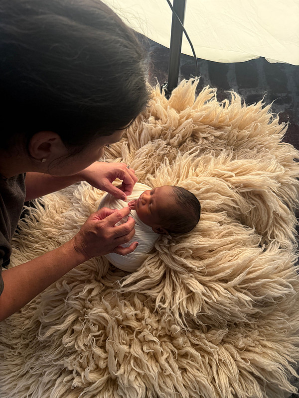Newborn photographer Teresa Carmouche gently adjusting a baby's white wrap during a newborn photography session in Gonzales, Louisiana.