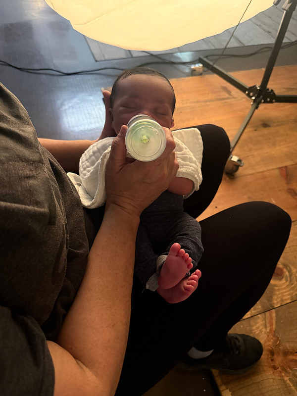 Newborn photographer Teresa Carmouche holding and bottle-feeding a newborn baby during a break in a studio photography session.