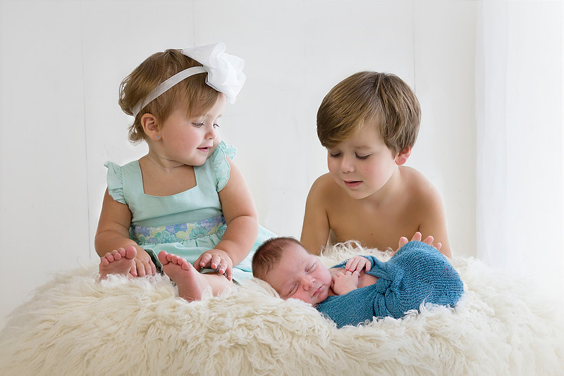 Three siblings photographed together in 2015, years before welcoming their newborn baby brother.