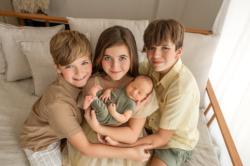 Three older siblings gathered around their newborn baby brother during a newborn photography session