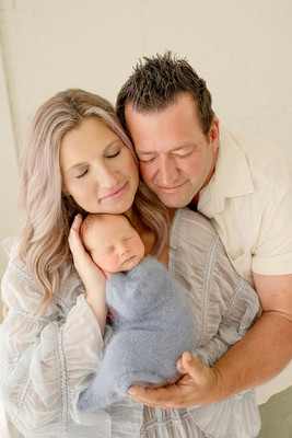 Mother and father cuddling their sleeping newborn son, dressed in a soft blue outfit.