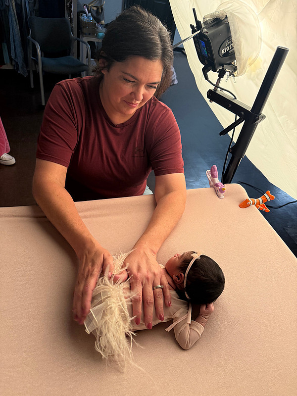 Newborn photographer Teresa Carmouche gently adjusting a baby's outfit while the newborn rests on a posing table in her Gonzales, Louisiana studio.