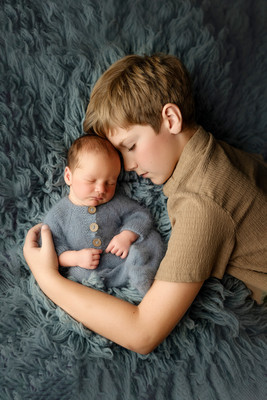 Big brother lying on a blue blanket, touching foreheads with his newborn baby brother