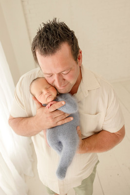 Father holding his sleeping newborn son close, with his cheek resting gently against the baby's head.